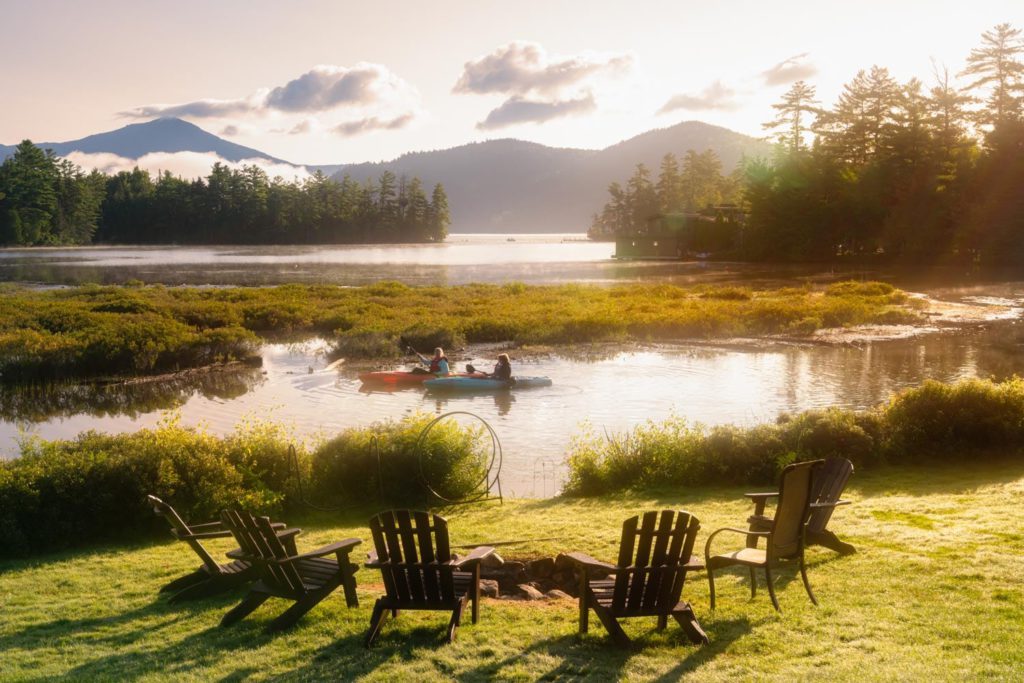 A lake with chairs and a fire pit in the background.