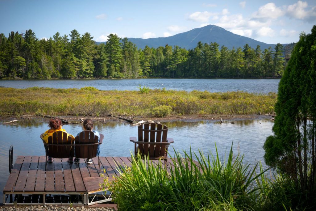 Two people sitting on a dock overlooking a lake.