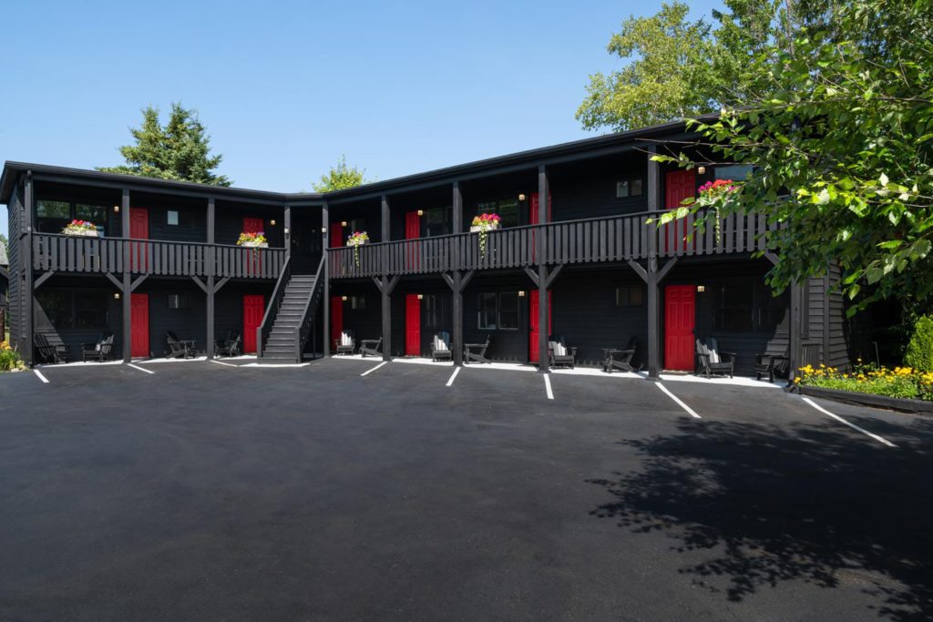 A black motel with red doors and a parking lot.