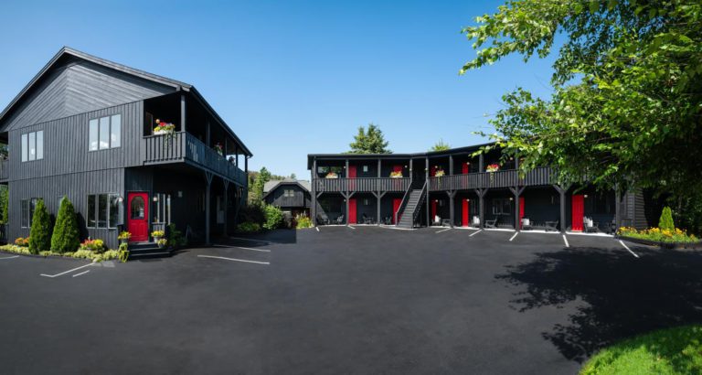 A black motel with red doors and a parking lot.