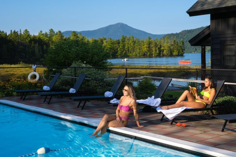 Two women in bikinis relaxing by a swimming pool.