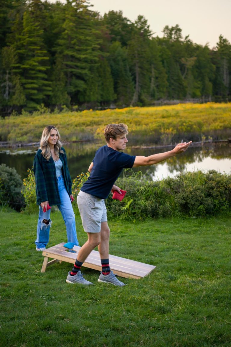 Two people playing a game of cornhole on a grassy field.