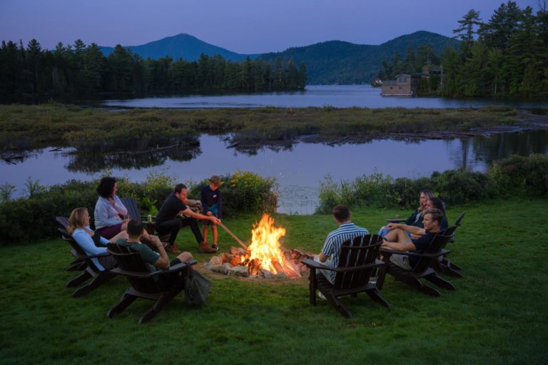 A group of people sitting around a fire pit in front of a lake.