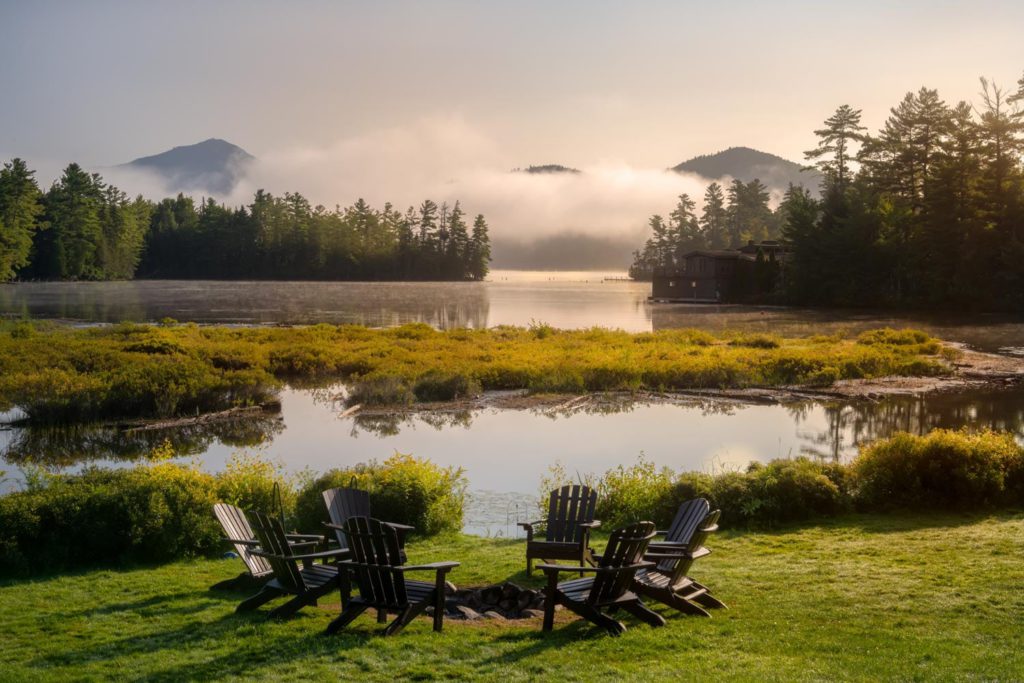 A group of lawn chairs in front of a lake with mist in the background.