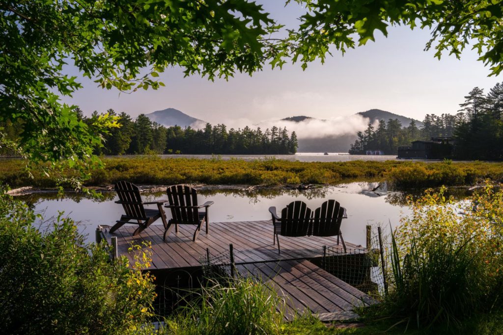 Two wooden chairs on a dock overlooking a lake.