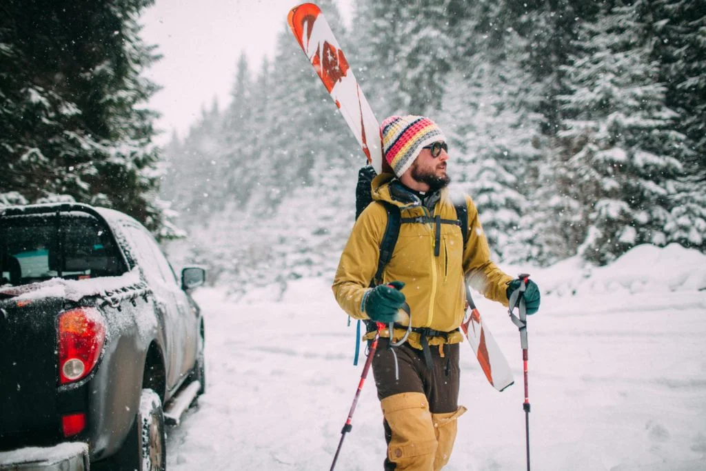 A man with skis walking down a snowy road.