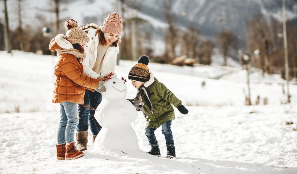 Three children playing with a snowman in the snow.