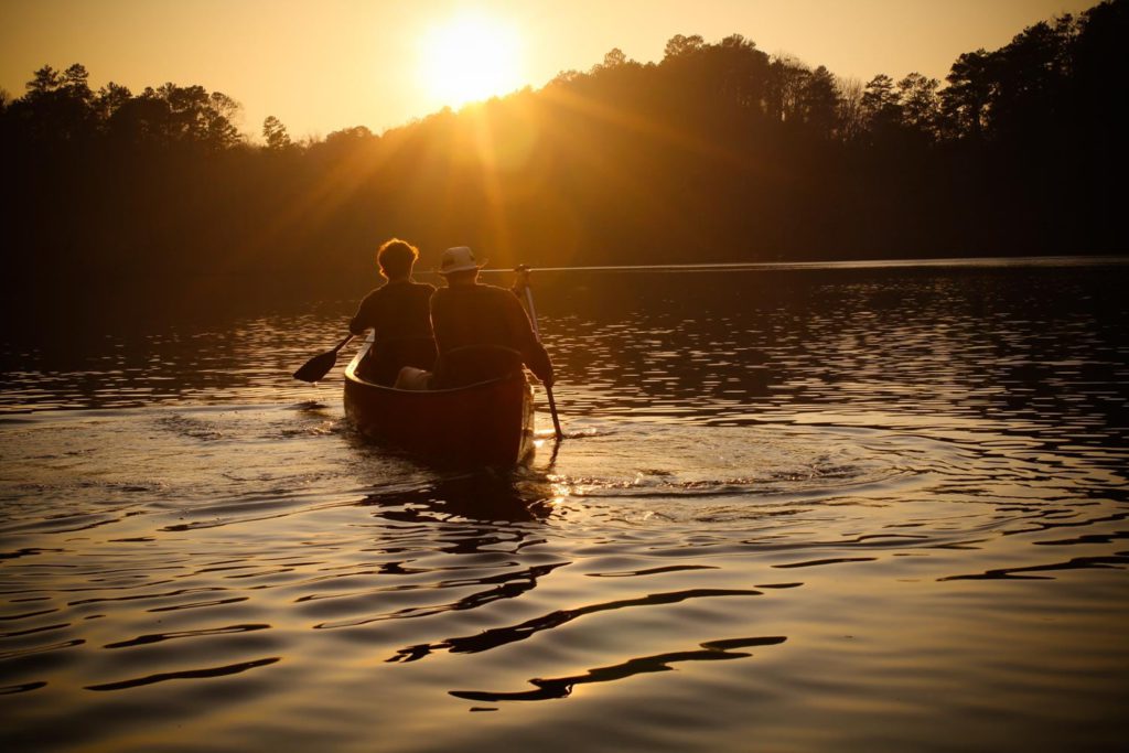 Two people paddling a canoe on a lake at sunset.