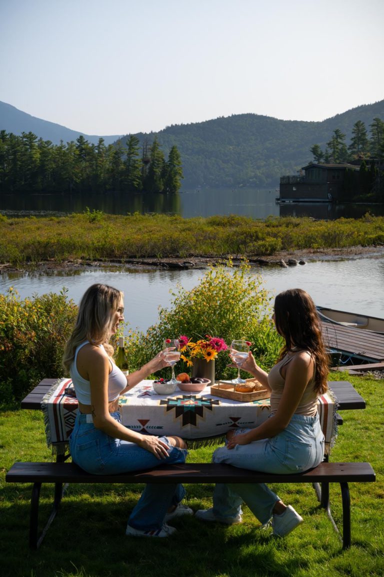 Two women sitting at a picnic table in front of a lake.