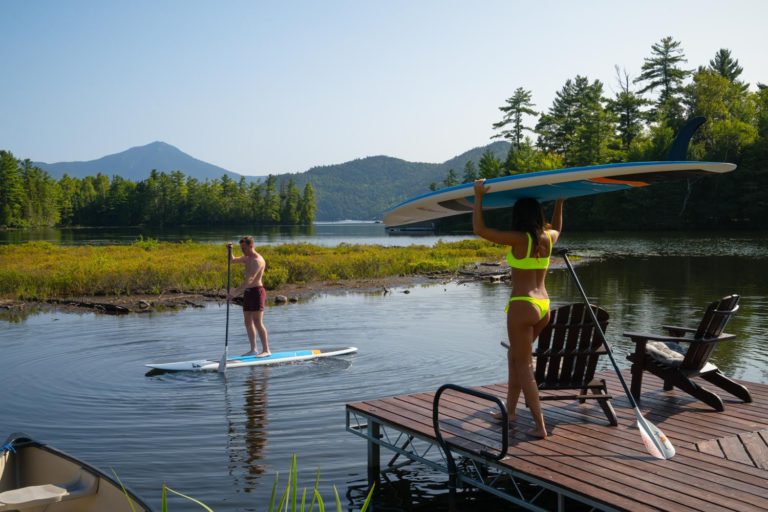 Two people stand up paddle boarding on a dock.