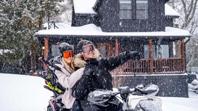 Two people on a snowmobile in front of a house.
