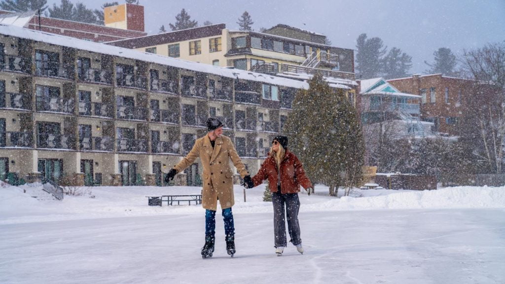 Two people ice skating on a frozen pond in front of a hotel.