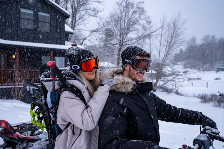 A couple wearing ski goggles and riding a snowmobile in the snow.