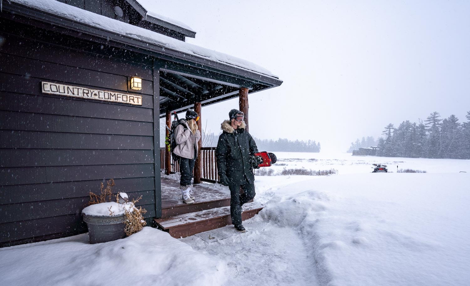 Two people standing on the steps of a cabin in the snow.