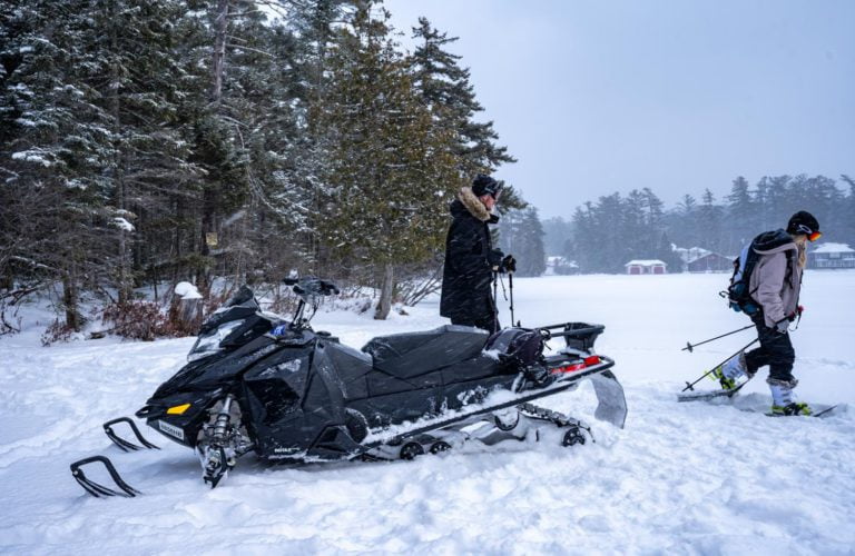 Two people standing next to a snowmobile in the snow.