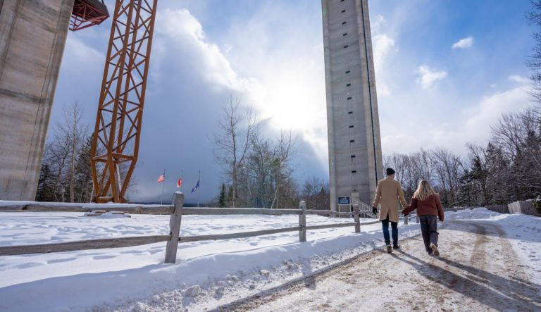 Two people walking down a snowy path near a tall building.