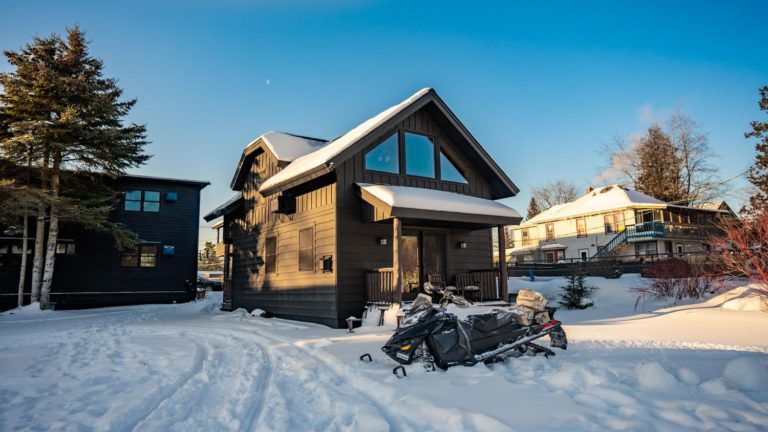 A small black house with a snowmobile parked in front of it.