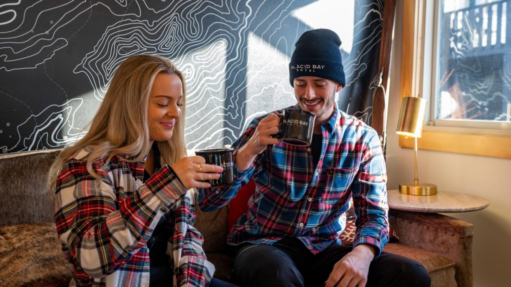 A man and woman sitting on a couch drinking coffee.