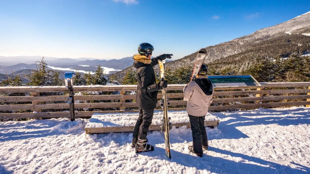 Two people standing on top of a snowy mountain with skis.