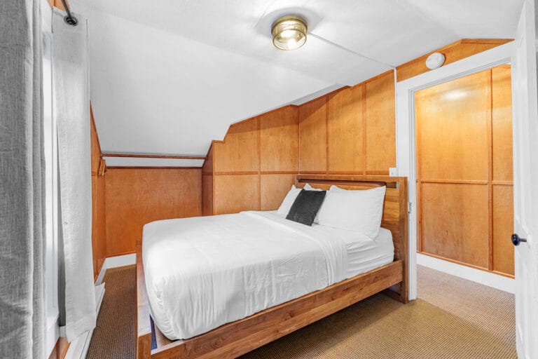 Small bedroom with wood-paneled walls, a bed with white linens, and a ceiling light.