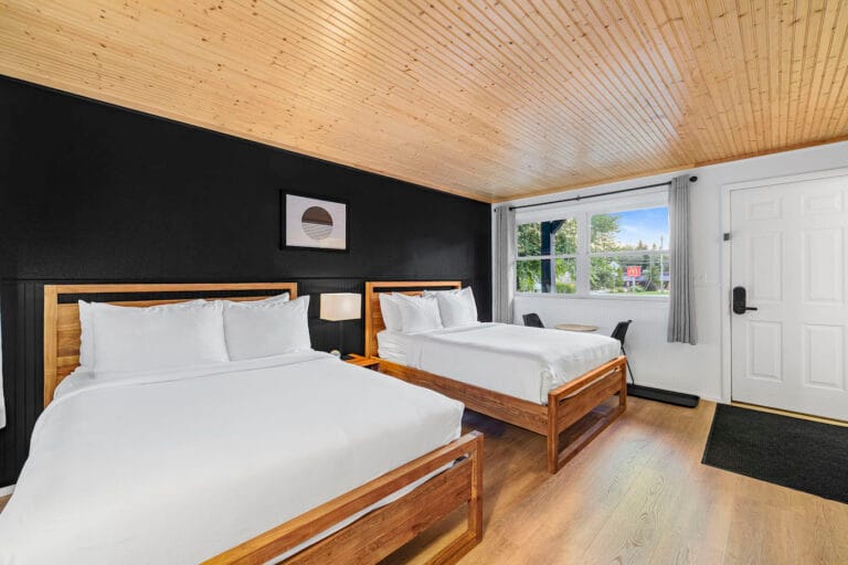 Room with two wooden beds, a black accent wall, wooden ceiling, and a large window.